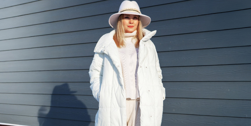 Woman staying warm on a windy day in a shiny black puffer jacket with comfortemp® insulation, under a cloudy blue sky.